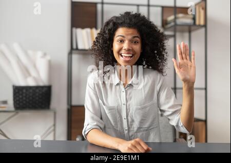 Young and energetic African-American female fresh graduate is ready for an online interview on a video call, sitting at the desk and looking and Stock Photo