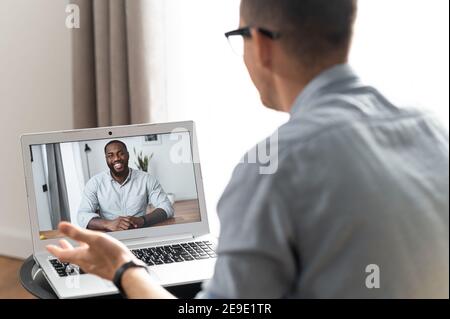 Video conference concept. Two collegues is talking via video connect, an African-American smiles on the laptop screen, chatting online, talk in the Stock Photo
