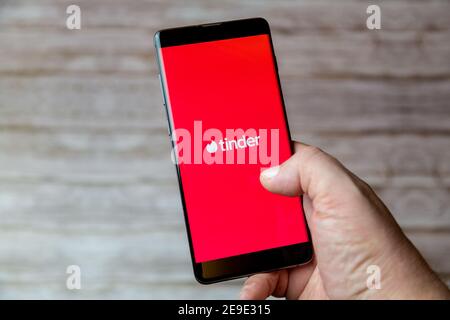 A hand holding a Mobile phone or cell phone with the Tinder online dating app on screen Stock Photo