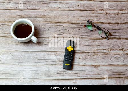 02-04-2021 Portsmouth, Hampshire, UK A Yellow Now TV remote control laid on a table or desk next to glasses and a coffee Stock Photo