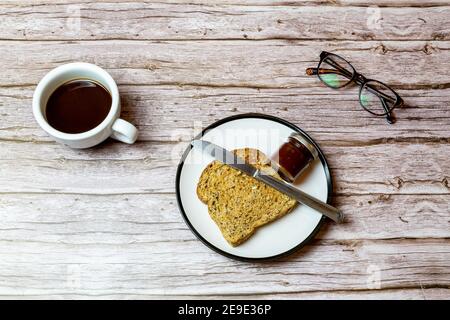 Toast and jam on a plate next to a coffee on a wooden table to represent breakfast time Stock Photo