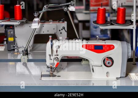 Professional sewing machine with spools of red threads close-up on the background of a sewing workshop in blur. Stock Photo