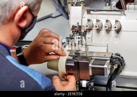 The hands of an old master set up a modern electric sewing machine and check the quality of the stitching. Stock Photo