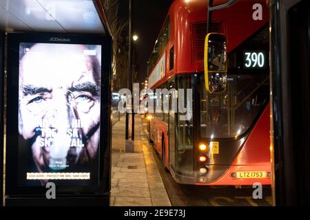 A government NHS (National Heath Service) ad at a bus stop displays the face of a Covid patient, urging Londoners to stay at home and to socially distance, outside the Royal Courts of Justice, on 2nd February 2021, in London, England. Stock Photo