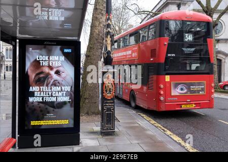 A government NHS (National Heath Service) ad at a Bus stop near the Royal Courts of Justice displays the face of a Covid patient, urging Londoners to stay at home and to socially distance, outside the Royal Courts of Justice, on 3rd February 2021, in London, England. Stock Photo