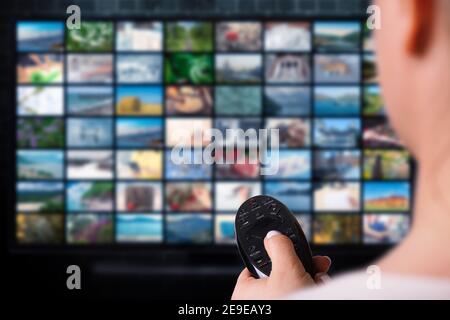woman hold remote control video service on demand on background TV with VOD provider icon. Online Media TV video. Video service with internet streamin Stock Photo