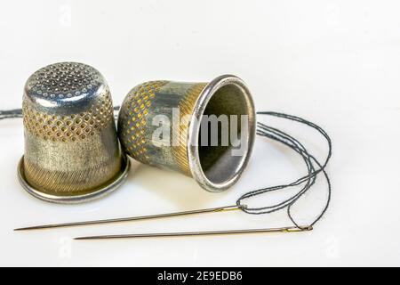 Two sewing needles with black thread and two sewing thimbles lie on a white background Stock Photo