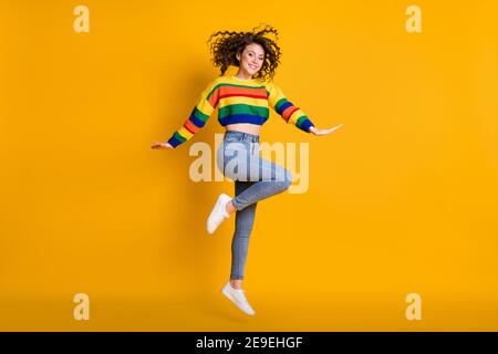 Full length photo of jumping lady wearing casual colorful sweater dancing pointing standing one leg isolated yellow color background Stock Photo