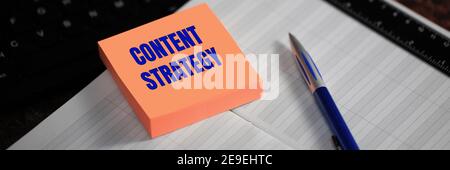 Content strategy. The text is written on a yellow sticker next to the pen and diary. Digital Marketing Media Concept Stock Photo