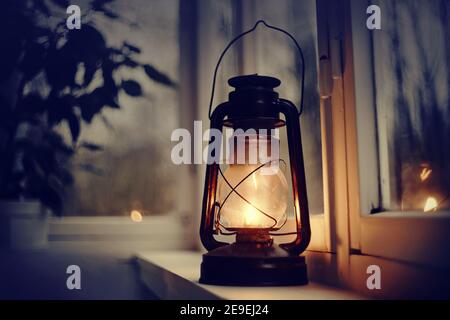 Vintage kerosene lamp stands on a white windowsill in the evening Stock Photo