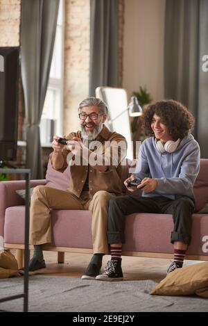 Happy father sitting on sofa and playing video game on TV together with his son at home Stock Photo