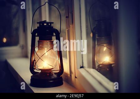Vintage kerosene lamp stands on a white windowsill in the evening Stock Photo