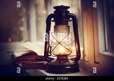 Kerosene lamp and old books on the windowsill. Stock Photo