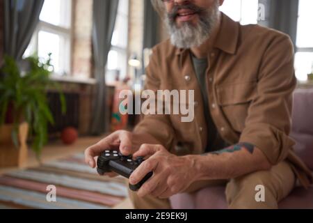 Close-up of bearded man holding joystick playing video game alone at home Stock Photo