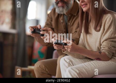 Close-up of couple using joysticks and playing online video games on the sofa in the room Stock Photo