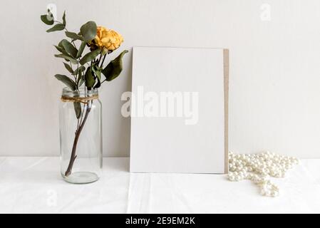 Fashionable stock stationery background - white card for lettering and dry yellow roses on a white table. Wedding feminine background. Blank for an in Stock Photo