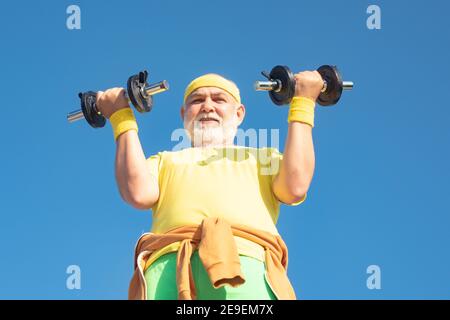 Senior fitness man training with dumbbells isolated on blue background. Senior man in gym working out with weights. Senior man lifting weights. Stock Photo