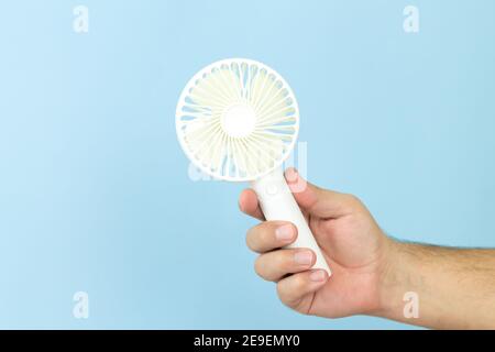 Man holding small portable usb fan close-up isolated on blue background Stock Photo
