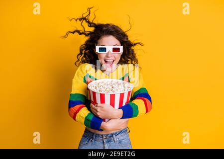 Photo of amazed funky young brunette hair lady hold popcorn watch tv wear spectacles sweater jeans isolated on yellow color background Stock Photo