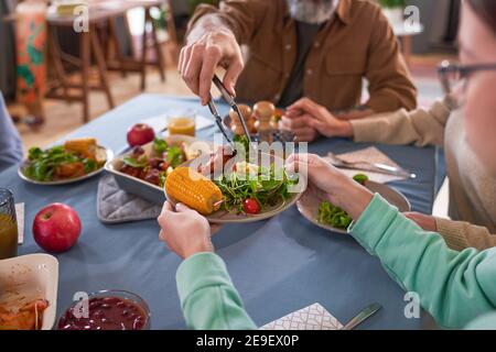 Close-up of family having dinner at the table in dining room they putting the salad on the plate Stock Photo