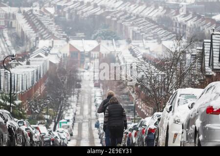A senior couple walking down on a London street covered by snow around Crouch End area as the capital experiences a rare covering of snow Stock Photo