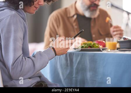 Close-up of boy sitting at dining table and using mobile phone during dinner Stock Photo