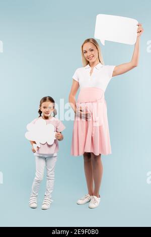 full length of pregnant mother and happy kid holding thought and speech bubbles on blue Stock Photo