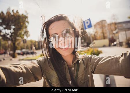 Photo of cute shiny charming young lady wear brown shirt dark glasses smiling making selfie outside sunny street Stock Photo
