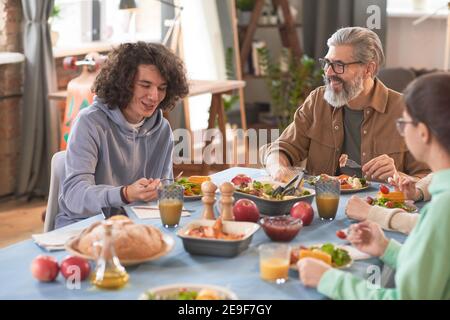 Happy family talking to each other while sitting at the table and having dinner at home Stock Photo