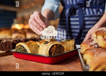 Sales Assistant In Bakery Putting Vegan Label Into Freshly Baked Baked Savoury Roll Stock Photo