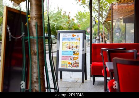 A sidewalk cafe in Paris France sits empty with a tourist menu board in front advertising crepes, breakfast and snacks Stock Photo