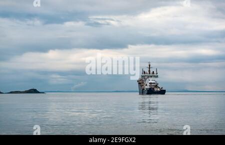 Moody view of supply ship in calm water with cloudy sky, Firth of Forth, Scotland, UK Stock Photo