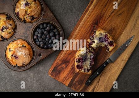 Freshly baked blueberry muffins with one on a cutting board with a bite taken out of it Stock Photo