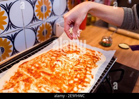 Hand sprinkling grated cheese over the tomato and a dough. Preparing a pizza. Stock Photo