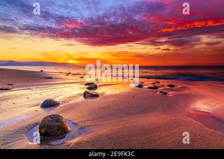 A Colorful Ocean Sunset With Rocks on the Beach and a Vibrant Cloudscape Overhead in the Sunset Sky Stock Photo