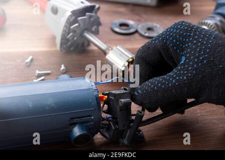 Power tool repair. Details of electrical appliance and repair tools on a wooden table in a repair shop. Stock Photo