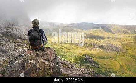 Young woman in sports clothing sitting on rocks enjoying the scenery of Andringitra national park, large stones massif background, during hike to pic Stock Photo