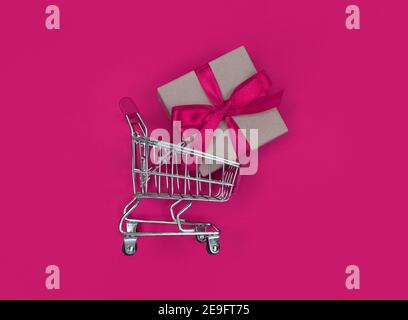 Supermarket trolley and gift box on pink background. Shopping concept. Stock Photo