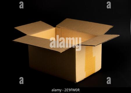 Opened cardboard packaging with mystic shining golden light in front of a dark black background. A brown carton box used for shipping and delivery Stock Photo