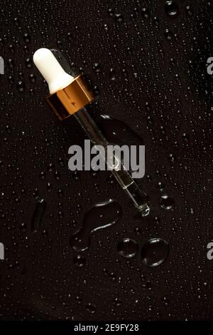 Glass tincture bottle with medicine dropper on black and blue background with drops of liquid and splashes on reflective surface. Medical lab tests. I Stock Photo