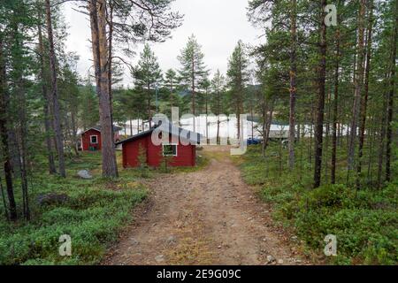 Stunning remote red wooden cabin in Inari, Lapland, Finland. Log is surrounded by idyllic green pine forest and romantic lake in the wilderness Stock Photo