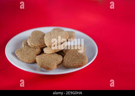 Heart shaped bistuits on a white dish on a red background, 45 degrees view Stock Photo