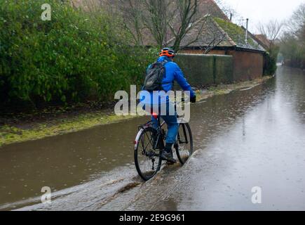 Sonning, Berkshire, UK. 4th February, 2021. A man cycles through floodwater near Sonning Bridge. Following heavy rain over the past few days, the River Thames has burst it's banks at Sonning in Berkshire. A Flood Alert is in place and low lying roads, paths and fields have flooded. Although the B478 across Sonning Bridge is closed due to the flooding, some drivers were ignoring the road closure signs and driving through the floods. Credit: Maureen McLean/Alamy Stock Photo
