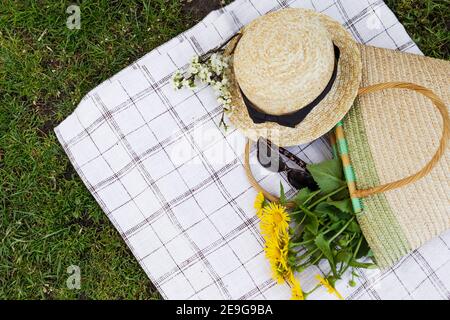 A bouquet of yellow flowers, sunglasses and a straw hat straw bag lie on the tablecloth. Top view. Stock Photo