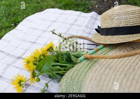 A bouquet of yellow flowers a straw hat and a straw bag lie on the tablecloth. Top view Stock Photo