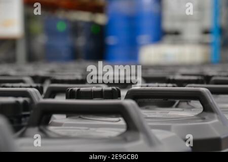 Tops of black plastic chemical containers in a warehouse with blue barrels of dangerous goods in the background Stock Photo