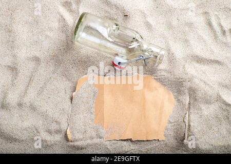 Gray blank paper covered with sand and a glass open bottle in the sand. The letter is on the beach. Summer season. Stock Photo