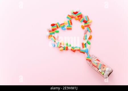 Heart made of colorful sugar candies on a pink background. Valentine's Day concept. Top view, flat lay. Stock Photo