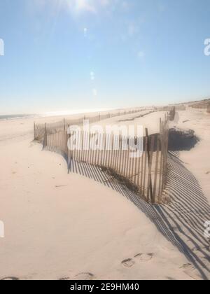 Sunny day at the New Jersey shore on a cold winter day. Snow fencing along the Jersey shore and the Atlantic Ocean. Long fence shadows on the beach. Stock Photo