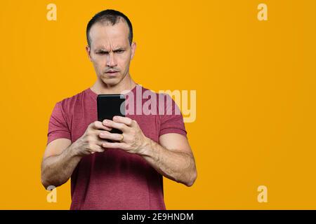 Mature Brazilian man looking at his smartphone and making a disapproving face. Orange background. Stock Photo